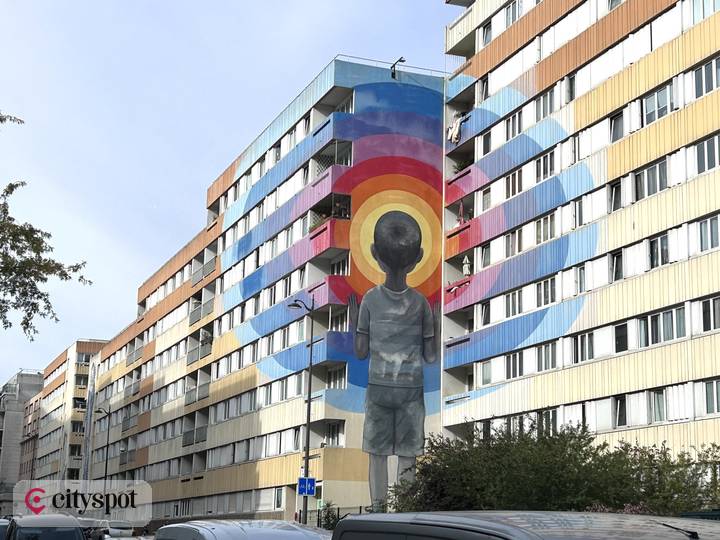 Seths Wandbild „Enter the Vortex“: ein Kind von hinten vor konzentrischen Regenbogenkreisen an einem Hochhaus